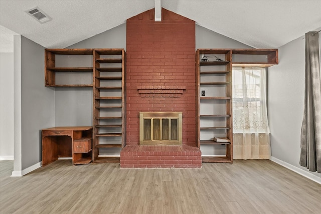 unfurnished living room with vaulted ceiling with beams, light wood-type flooring, a textured ceiling, and a brick fireplace