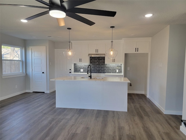 kitchen featuring backsplash, a center island with sink, sink, ceiling fan, and white cabinetry