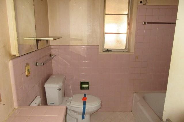 bathroom featuring toilet, tile walls, and a washtub