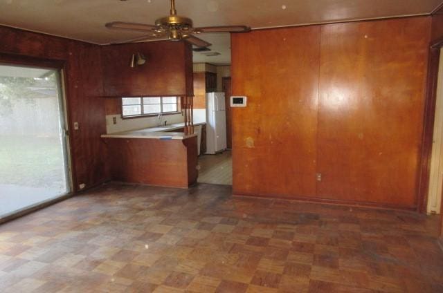 kitchen with white refrigerator, ceiling fan, and wood walls