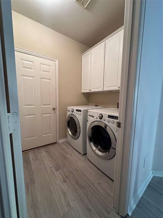 washroom with a textured ceiling, light hardwood / wood-style flooring, cabinets, and washing machine and clothes dryer