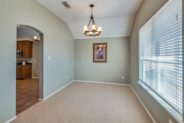 carpeted empty room with lofted ceiling and an inviting chandelier