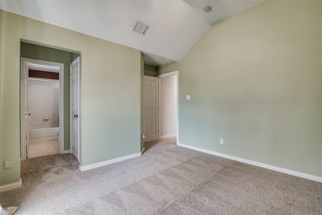 unfurnished bedroom featuring connected bathroom, light carpet, and lofted ceiling