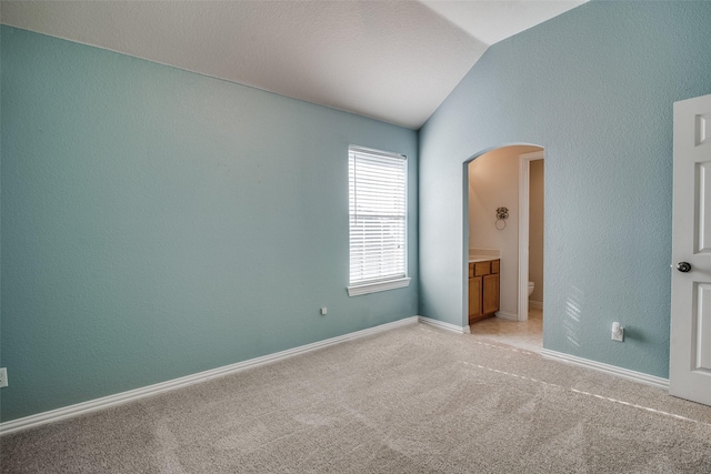 unfurnished bedroom with connected bathroom, light colored carpet, and vaulted ceiling