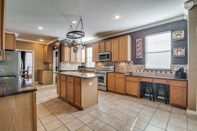 kitchen with a center island, crown molding, dark stone countertops, appliances with stainless steel finishes, and light tile patterned flooring