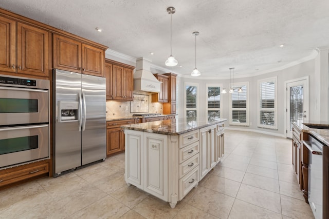 kitchen with light stone countertops, appliances with stainless steel finishes, custom exhaust hood, pendant lighting, and a kitchen island