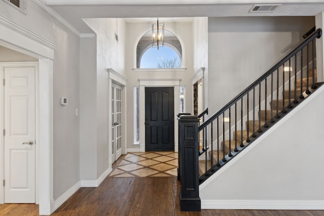 foyer entrance with a chandelier, a towering ceiling, dark wood-type flooring, and ornamental molding