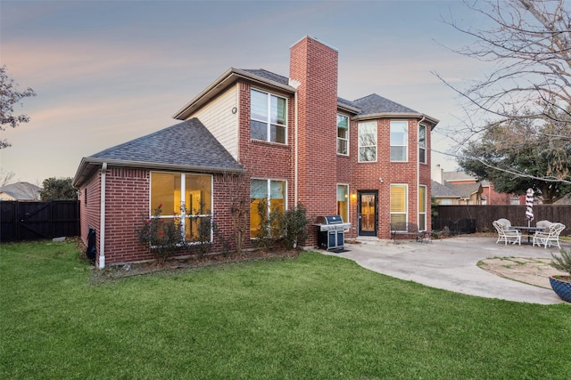 back house at dusk featuring a lawn and a patio area