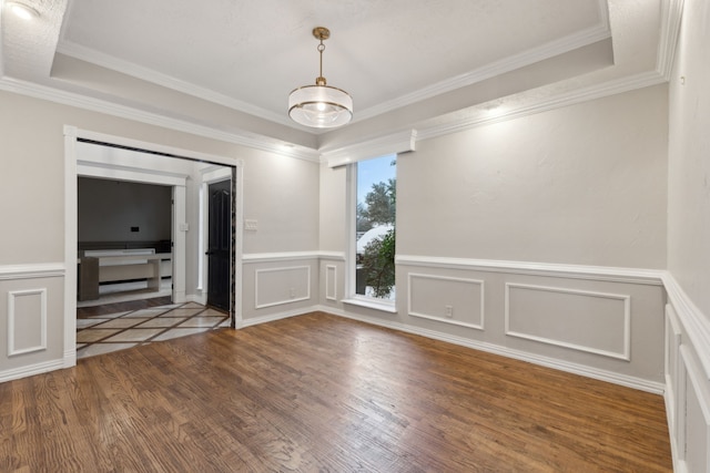 spare room featuring wood-type flooring, a raised ceiling, ornamental molding, and a notable chandelier