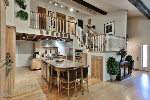 kitchen with a kitchen island, a towering ceiling, beamed ceiling, light stone countertops, and light wood-type flooring