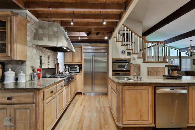 kitchen with sink, stone countertops, beamed ceiling, stainless steel appliances, and range hood