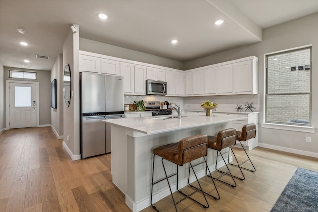 kitchen featuring stainless steel appliances, light hardwood / wood-style flooring, an island with sink, a breakfast bar area, and white cabinets