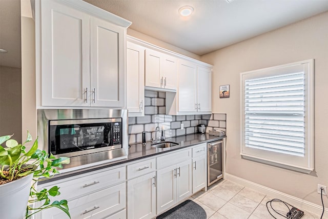 kitchen with stainless steel microwave, backsplash, beverage cooler, white cabinetry, and a sink