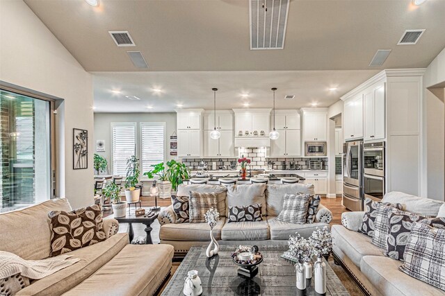 kitchen featuring stainless steel appliances, decorative light fixtures, white cabinetry, backsplash, and a center island with sink