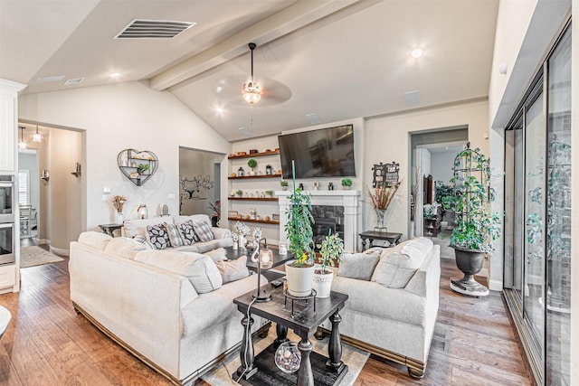 living room with visible vents, a ceiling fan, a tile fireplace, lofted ceiling with beams, and wood finished floors