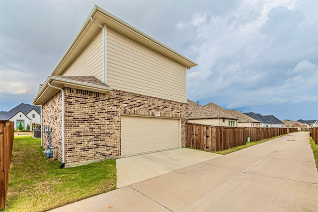 view of property exterior with fence, driveway, an attached garage, brick siding, and a residential view