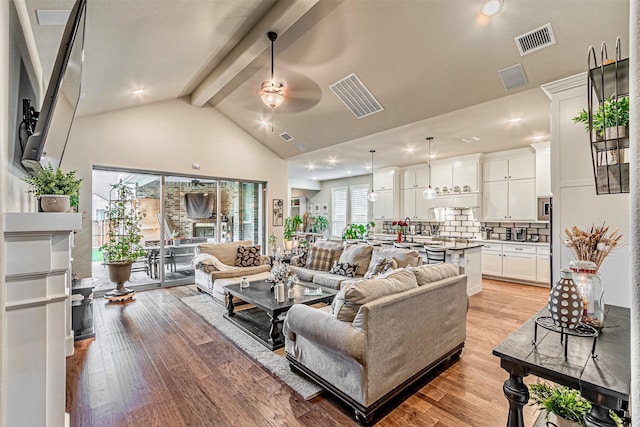 living room featuring beam ceiling, light wood-style flooring, visible vents, and ceiling fan