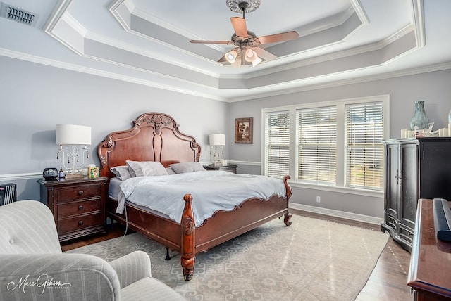 bedroom with crown molding, ceiling fan, a raised ceiling, and light wood-type flooring