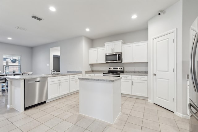 kitchen featuring white cabinets, sink, a kitchen island, light stone counters, and stainless steel appliances