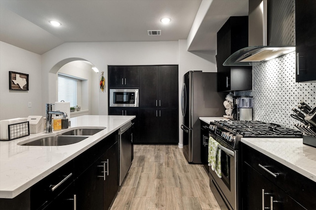 kitchen with sink, wall chimney range hood, vaulted ceiling, appliances with stainless steel finishes, and light wood-type flooring