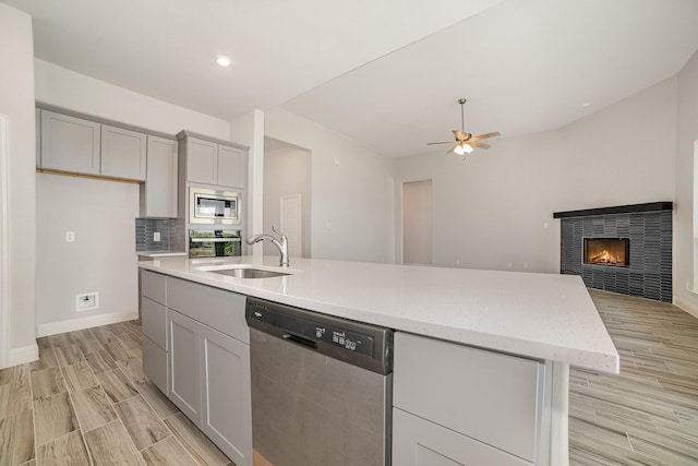 kitchen featuring appliances with stainless steel finishes, gray cabinetry, sink, a center island with sink, and a tiled fireplace