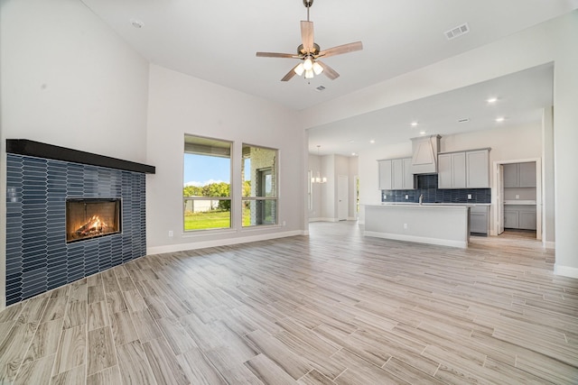 unfurnished living room with ceiling fan, a fireplace, sink, and light wood-type flooring