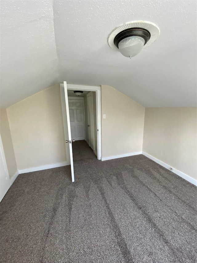 additional living space with vaulted ceiling, a textured ceiling, and dark colored carpet