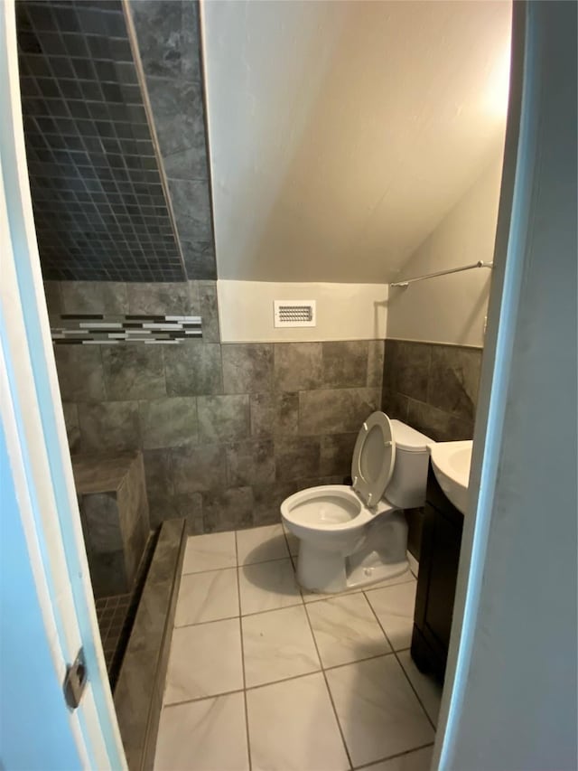 bathroom with vanity, tile patterned floors, toilet, tiled shower, and tile walls