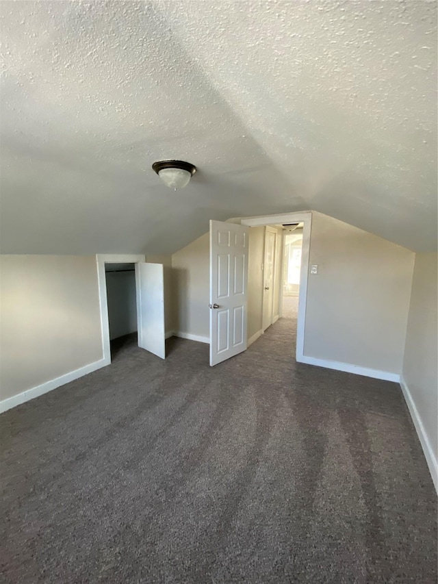 bonus room featuring vaulted ceiling, a textured ceiling, and dark colored carpet