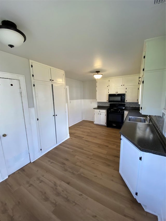 kitchen with dark wood-type flooring, white cabinets, black appliances, and sink