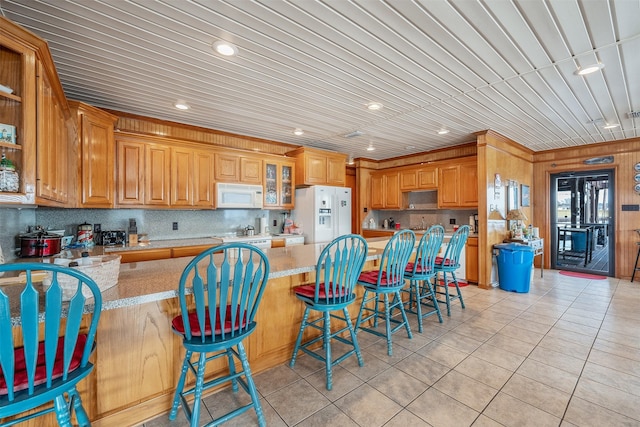 kitchen featuring kitchen peninsula, a kitchen breakfast bar, white appliances, light tile patterned floors, and wood walls