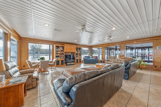 living room with wood walls, ceiling fan, a healthy amount of sunlight, and light tile patterned floors