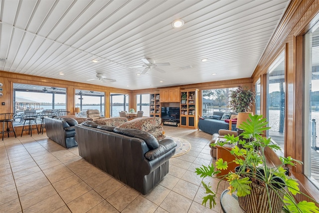 tiled living room with ceiling fan, a water view, wood ceiling, and wood walls