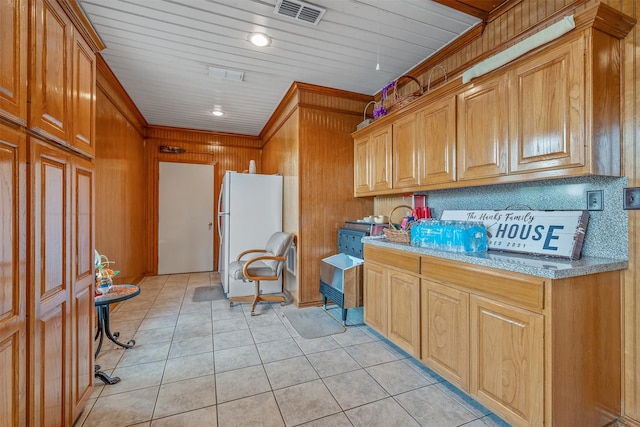 kitchen featuring light tile patterned flooring, white refrigerator, light stone countertops, and wood walls