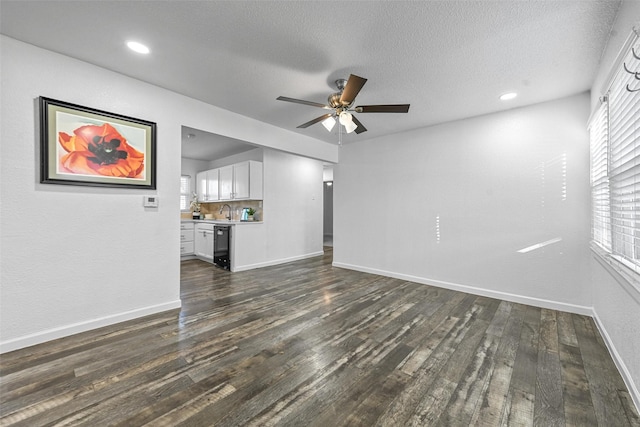 unfurnished living room featuring dark wood-type flooring, sink, a textured ceiling, and ceiling fan