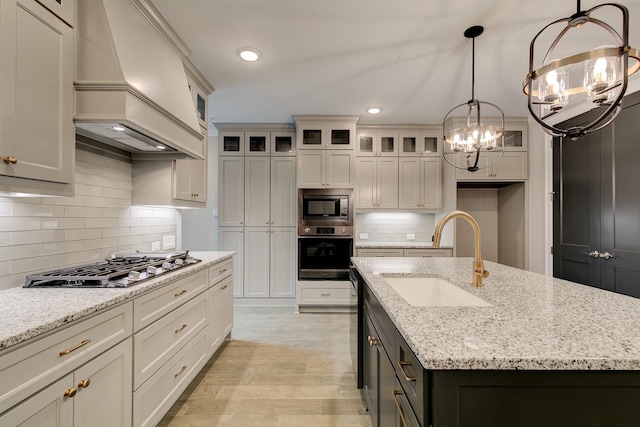 kitchen featuring custom exhaust hood, stainless steel appliances, a kitchen island with sink, and an inviting chandelier