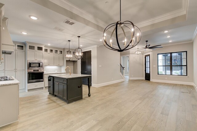 kitchen featuring ceiling fan with notable chandelier, stainless steel appliances, a kitchen island with sink, pendant lighting, and light hardwood / wood-style floors