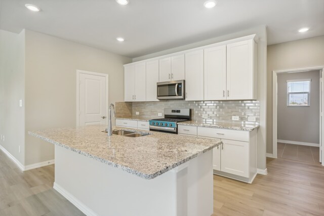 kitchen with sink, stainless steel appliances, an island with sink, white cabinets, and light wood-type flooring