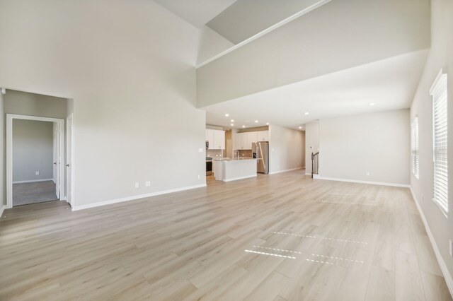 unfurnished living room with a high ceiling and light wood-type flooring