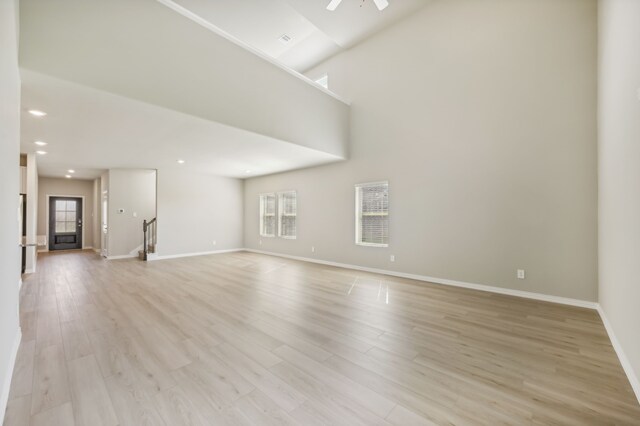 unfurnished living room with ceiling fan, light hardwood / wood-style flooring, a towering ceiling, and a healthy amount of sunlight