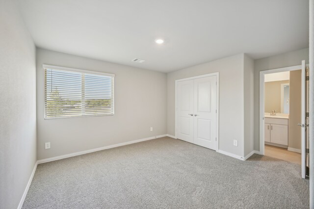 unfurnished bedroom featuring ensuite bathroom, a closet, light colored carpet, and sink