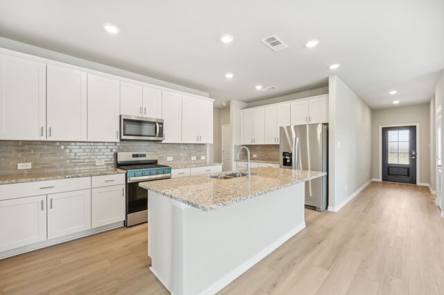 kitchen with appliances with stainless steel finishes, light wood-type flooring, sink, a center island with sink, and white cabinets