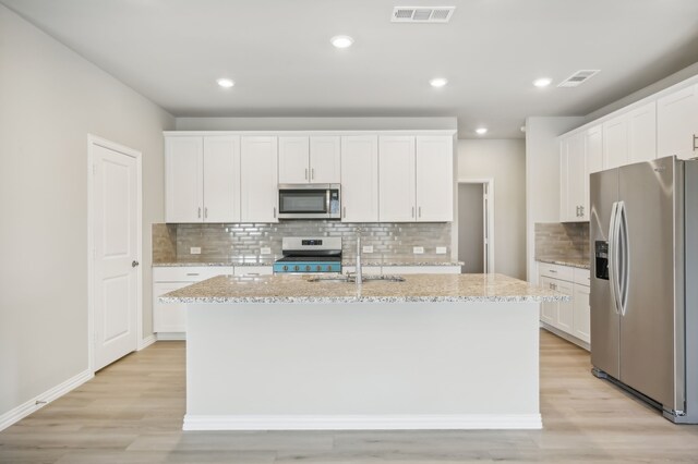 kitchen with white cabinets, sink, stainless steel appliances, and an island with sink