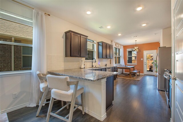 kitchen featuring dark brown cabinetry, tasteful backsplash, dark hardwood / wood-style floors, pendant lighting, and a breakfast bar area