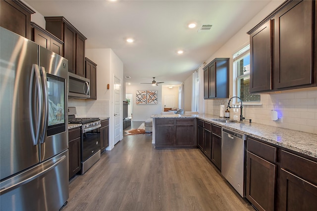 kitchen with light stone counters, stainless steel appliances, ceiling fan, sink, and hardwood / wood-style floors