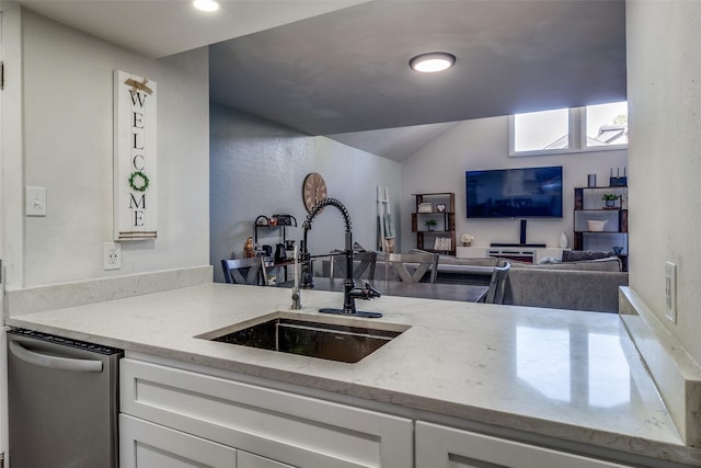 kitchen featuring light stone countertops, vaulted ceiling, sink, dishwasher, and white cabinetry