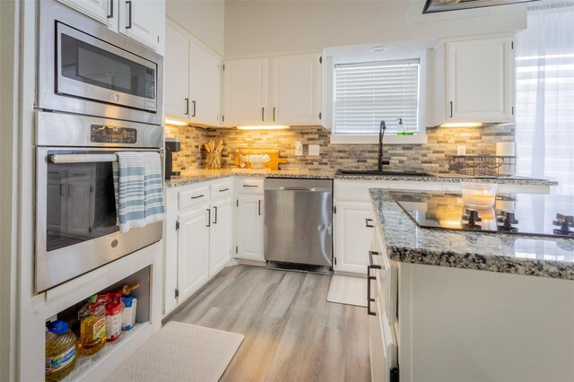 kitchen with appliances with stainless steel finishes, light stone counters, sink, white cabinets, and light hardwood / wood-style floors