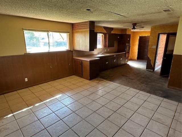 kitchen with a textured ceiling, sink, oven, and wood walls