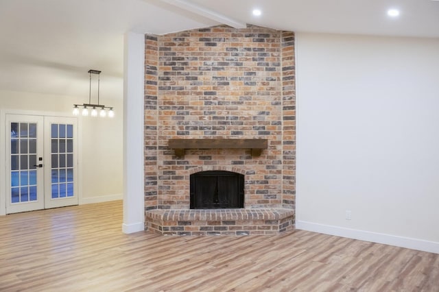 unfurnished living room with a brick fireplace, lofted ceiling with beams, light wood-type flooring, and french doors