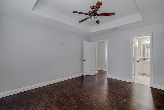 unfurnished bedroom featuring dark hardwood / wood-style floors, connected bathroom, sink, ceiling fan, and a tray ceiling